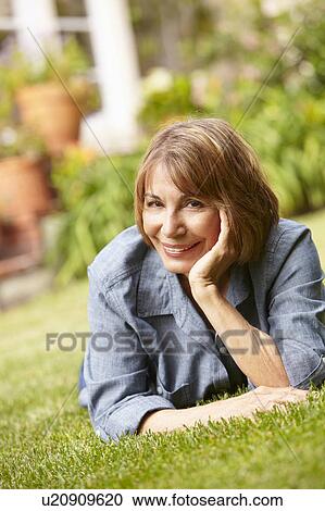 Stock Image - Mid age woman relaxing in garden. Fotosearch
