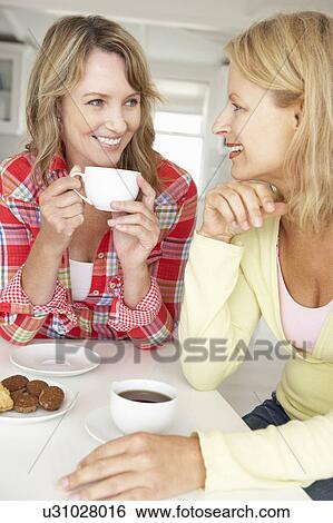 Stock Photograph - Mid age women chatting over coffee at home. Fotosearch