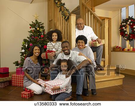 Stock Image - Mixed race family with Christmas tree and gifts. Fotosearch