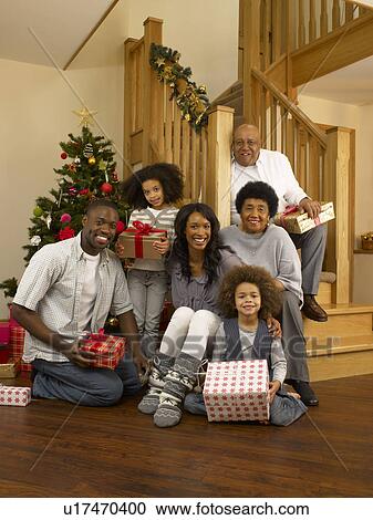 Stock Image - Mixed race family with Christmas tree and gifts. Fotosearch