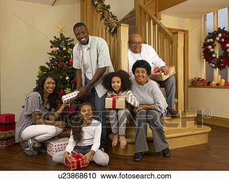 Stock Image - Mixed race family with Christmas tree and gifts. Fotosearch