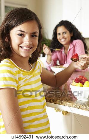 Stock Image - Mother and daughter eating cereal and fruit. Fotosearch