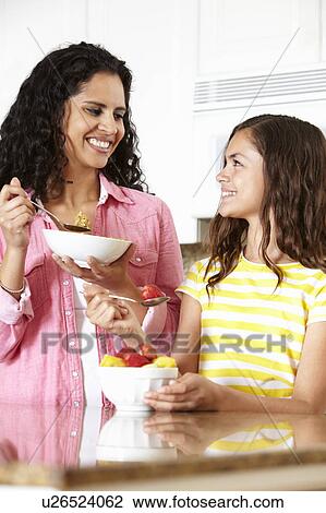 Stock Image - Mother and daughter eating cereal and fruit. Fotosearch