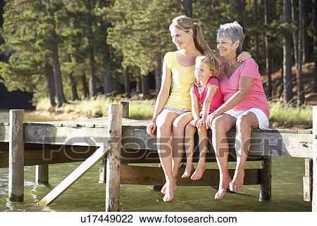 Stock Image - Mother, daughter and grandmother sitting by lake. Fotosearch