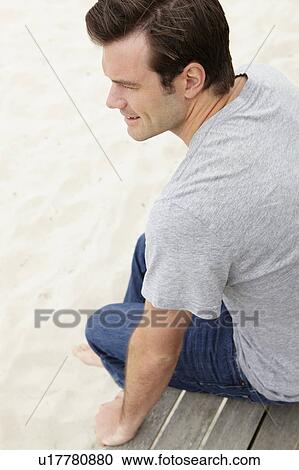 Stock Image - Portrait man sitting by beach. Fotosearch