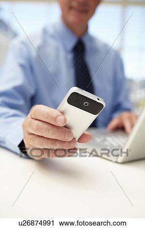 Stock Image - Senior businessman with laptop and phone. Fotosearch
