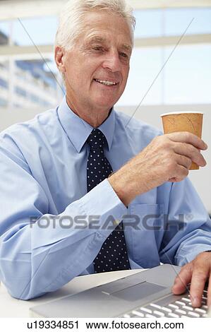Stock Image - Senior businessman with laptop and coffee. Fotosearch