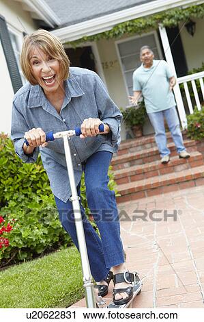 Stock Image - Senior couple playing with children's scooter. Fotosearch