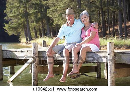 Stock Image - Senior couple sitting by lake. Fotosearch