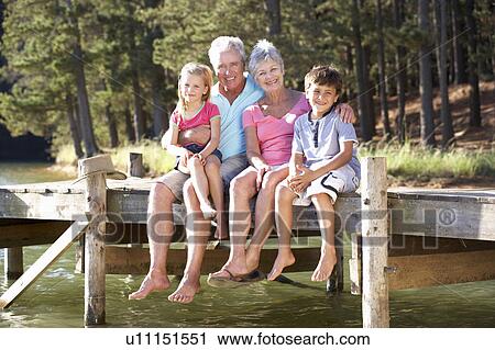 Stock Image - Senior couple sitting by lake with grandchildren. Fotosearch
