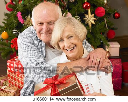 Picture - Senior couple with gifts in front of Christmas tree. Fotosearch