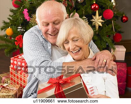 Stock Image - Senior couple with gifts in front of Christmas tree. Fotosearch