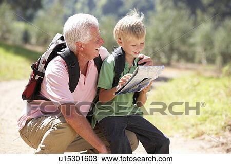 Stock Image - Senior man reading map with grandson on country walk. Fotosearch