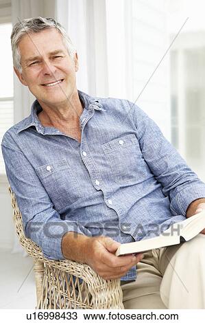 Stock Image - Senior man relaxing at home with a book. Fotosearch