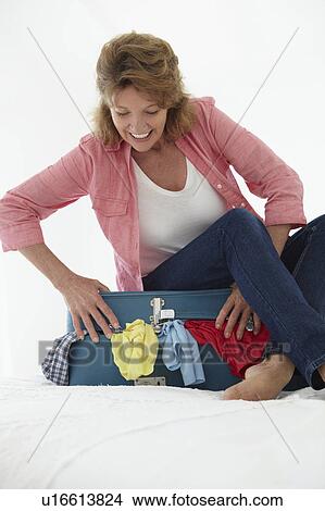 Picture - Senior woman struggling to close suitcase. Fotosearch