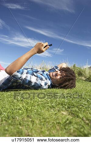 Teenage boy lying on grass with phone View Large Photo Image Stock Image - Teenage boy lying on grass with phone. Fotosearch