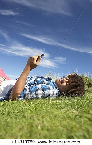 Teenage boy lying on grass with phone View Large Photo Image Stock Photo - Teenage boy lying on grass with phone. Fotosearch