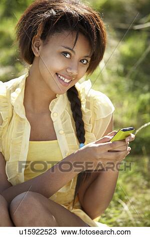 Stock Image - Teenage girl using phone outdoors. Fotosearch
