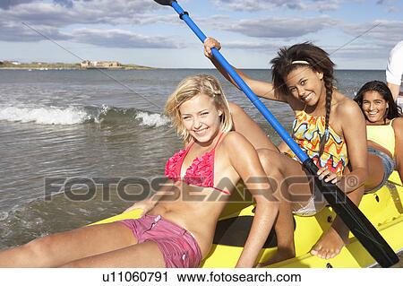 Stock Image - Teenage girls in sea with canoe. Fotosearch