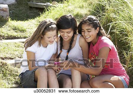 Stock Image - Teenage girls using phone outdoors. Fotosearch