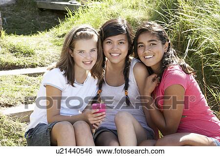 Stock Photograph - Teenage girls using phone outdoors. Fotosearch