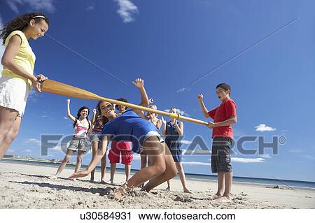 Stock Image - Teenagers doing limbo dance on beach. Fotosearch