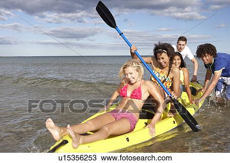 Stock Image - Teenagers in sea with canoe. Fotosearch