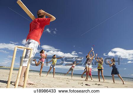 Stock Image - Teenagers playing cricket on beach. Fotosearch