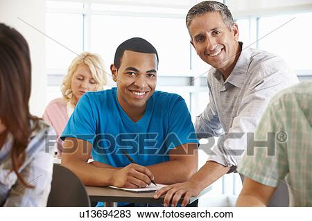 Stock Image - Tutor helping student in class. Fotosearch