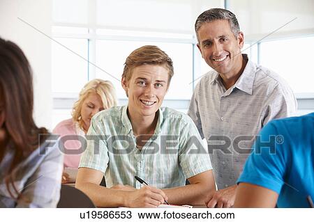 Stock Image - Tutor helping student in class. Fotosearch
