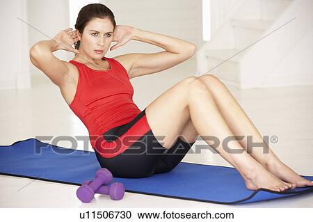 Stock Image - Woman doing sit-ups in home gym. Fotosearch