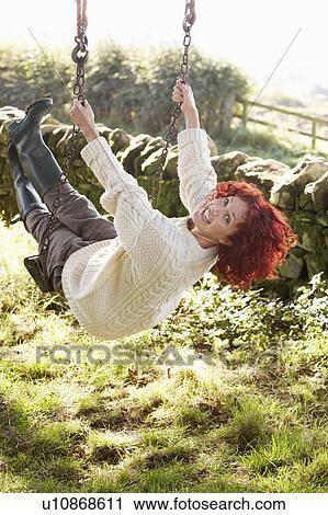 Stock Image - Woman on country garden swing. Fotosearch
