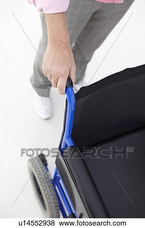 Stock Photo - Woman pushing empty wheelchair. Fotosearch