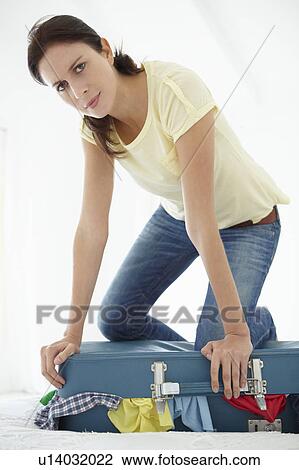 Stock Image - Woman struggling to close suitcase. Fotosearch