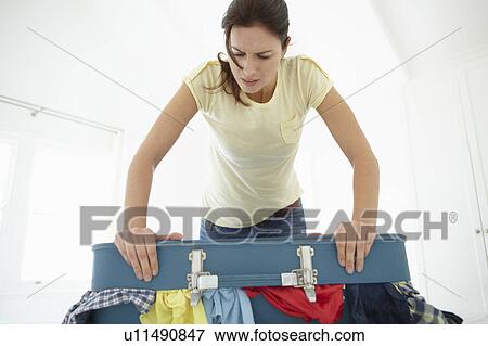 Stock Photo - Woman struggling to close suitcase. Fotosearch