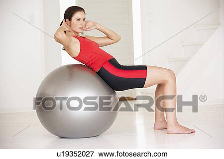 Stock Photo - Woman with gym ball in home gym. Fotosearch