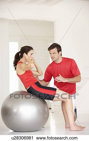 Stock Image - Woman with personal trainer in home gym. Fotosearch