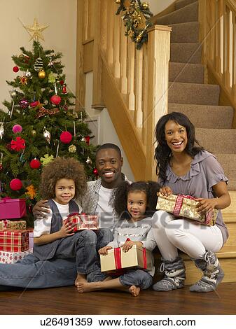 Stock Photo - Young African American family with Christmas tree and gifts. Fotosearch