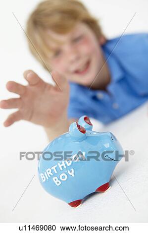 Stock Image - Young boy reaching for piggy bank. Fotosearch