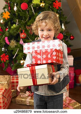 Stock Photo - Young child holding gifts in front of Christmas tree. Fotosearch