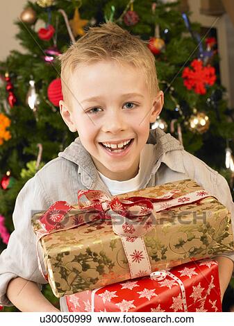 Stock Photo - Young child holding gifts in front of Christmas tree. Fotosearch