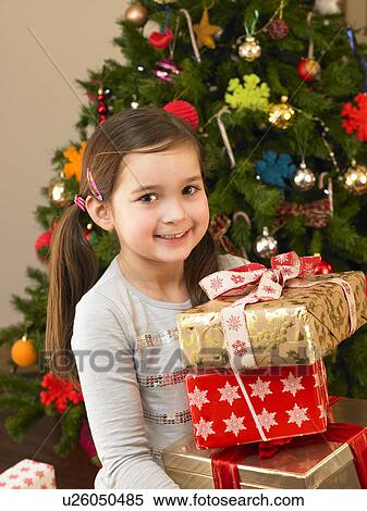 Stock Photography - Young child holding gifts in front of Christmas tree. Fotosearch