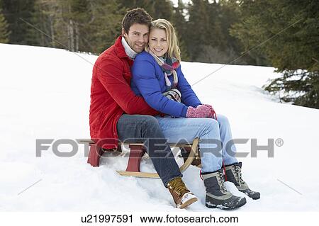 Stock Image - Young Couple On A Sled In Alpine Snow Scene. Fotosearch