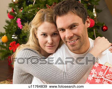 Young couple with gifts in front of Christmas tree View Large Photo Image Stock Photo - Young couple with gifts in front of Christmas tree. Fotosearch