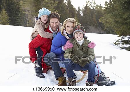 Stock Image - Young Family Sitting On A Sled In The Snow. Fotosearch