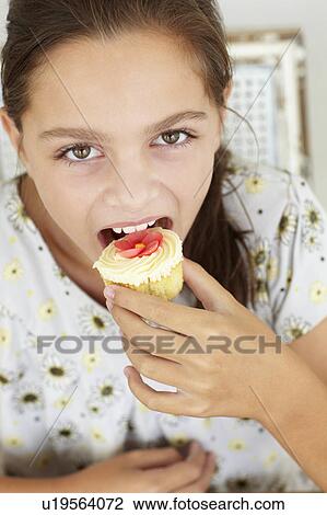 Stock Image - Young girl eating cupcake. Fotosearch