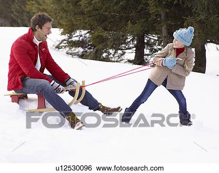 Stock Photograph - Young Girl Pulling Father Through Snow On Sled. Fotosearch