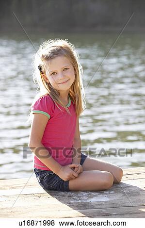 Stock Photo - Young girl sitting by lake. Fotosearch