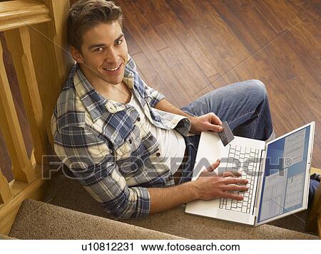 Stock Image - Young Hispanic man shopping online. Fotosearch