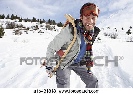 Stock Photo - Young Man Carrying Sled In Alpine Landscape. Fotosearch